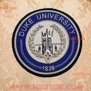 May include: A circular embroidered patch featuring the text DUKE UNIVERSITY and 1838 in silver thread on a blue background. The center displays a white field with a silver embroidered building silhouette surrounded by a silver laurel wreath.