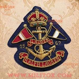 May include: A navy blue embroidered patch featuring a gold crown, a central anchor, and two crossed flags in red and blue with white stripes. The text reads LAUREN, 19, 67, and RALPH LAUREN in gold thread against the dark blue felt background.