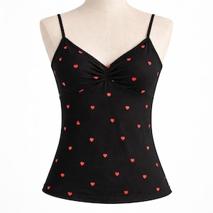 Op de afbeelding: Zwarte camisole met een rood hartjespatroon. De top heeft een V-hals en dunne spaghettibandjes. De stof is bij de buste gerimpeld. De hartjes zijn gelijkmatig verdeeld.