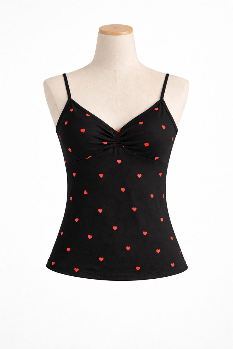 Op de afbeelding: Zwarte camisole met een rood hartjespatroon. De top heeft een V-hals en dunne spaghettibandjes. De stof is bij de buste gerimpeld. De hartjes zijn gelijkmatig verdeeld.