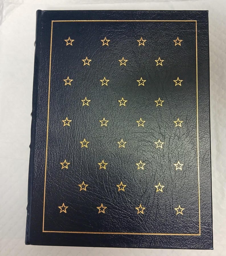 May include: A navy blue book with a gold border and gold star pattern. The cover has a textured appearance. The spine is visible on the left side.