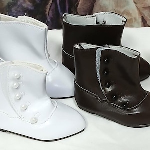 Puede incluir: Una colección de botines para muñecas en varios colores, incluyendo negro, blanco, marrón y crema. Los botines tienen detalles de botones y perlas, con un diseño clásico de botín. Los botines están colocados sobre una superficie blanca.