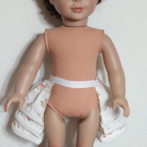 May include: A doll wearing a peach-colored sleeveless leotard with a white waistband and a white and pink floral skirt.