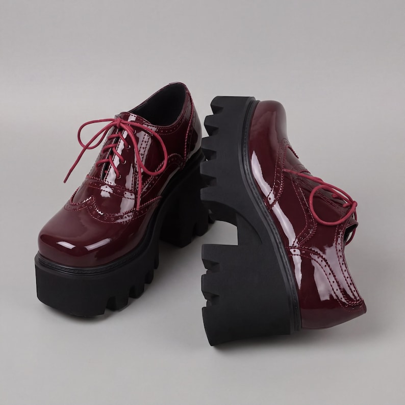 Pode incluir: Um par de sapatos Oxford de plataforma bord&ocirc; com acabamento brilhante. Os sapatos apresentam um design com atacadores com atacadores bord&ocirc; a condizer e uma sola grossa e preta com rasto. Fundo cinzento claro.