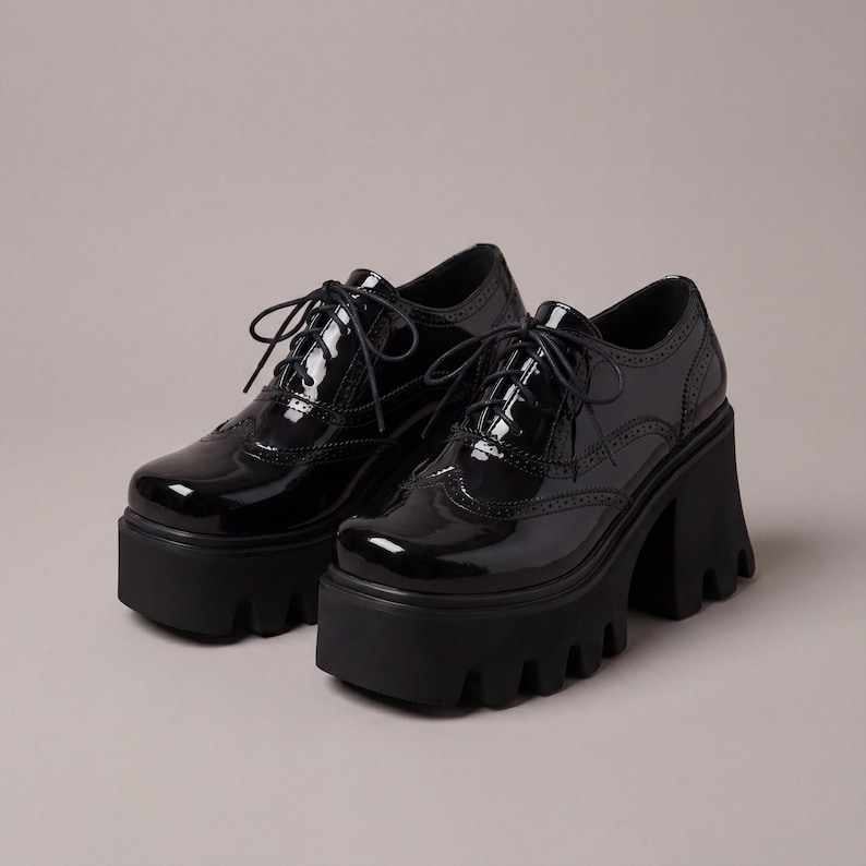 Pode incluir: Um par de sapatos oxford pretos com plataforma e acabamento brilhante. Os sapatos apresentam um design com atacadores, perfura&ccedil;&otilde;es decorativas e uma sola grossa e com rasto. Os saltos t&ecirc;m cerca de 10 cm de altura.