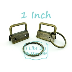 May include: Antique brass-colored purse hardware set. Includes two rectangular clasps with a 1-inch (2.54 cm) opening and a key ring. The text "1 Inch" is displayed above the hardware. The text "I Like Big Buttons!" is also visible.