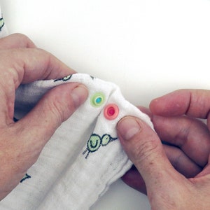 May include: A white fabric baby blanket with a green and black bird design. The blanket has two snaps, one green and one pink.