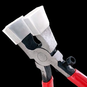 May include: Close-up of a pair of red-handled pliers with white rubber jaws. The pliers are used for crimping metal.