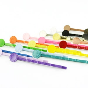 May include: A collection of colorful bobby pins with round, flat, decorative tops. The pins are arranged diagonally across a white background, showcasing a variety of colors including green, orange, pink, yellow, red, and purple. The bobby pins are for hair styling.