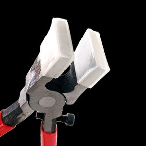 May include: Close-up of a pair of red-handled pliers with two white, rectangular jaws. The jaws are open and ready to grip.