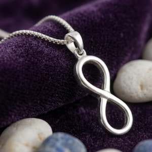 May include: A silver-toned infinity symbol pendant suspended from a matching box chain necklace. The pendant features a smooth, polished metallic finish and is shaped as a continuous loop, representing the mathematical sign for infinity.