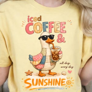 May include: Yellow t-shirt with a graphic of a duck wearing sunglasses, drinking iced coffee. The text reads "iced COFFEE & SUNSHINE all day, every day". The duck has patchwork wings and is standing on a starfish and seashell.