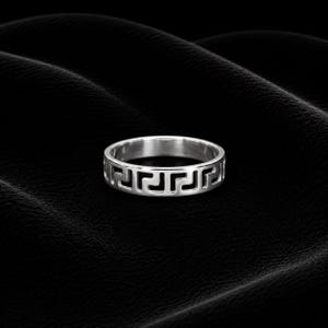 Könnte beinhalten: Ein silberner Ring mit einem griechischen Schlüsselmuster. Der Ring ist kreisförmig mit einem durchgehenden geometrischen Design um das Band. Er ist vor einem dunklen, strukturierten Hintergrund platziert, der seinen metallischen Glanz hervorhebt.