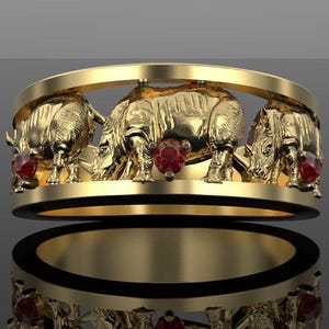 Peut inclure: Une bague en or avec une série de figurines de rhinocéros sculptées intégrées au design. La bague est ornée de trois petites pierres précieuses rouges, rondes et facettées, placées entre les rhinocéros tout autour de l'anneau.
