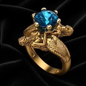 May include: A gold ring featuring two sculpted mermaid figures with detailed scales along the band. The figures support a large, round, faceted blue gemstone held in a prong setting at the center of the ring, creating a decorative design.