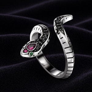 May include: Silver snake ring with black, red, and green gemstones. The snake's head features a teardrop-shaped red stone, a small green stone, and black stones. The ring's body is detailed with black stones and a textured design.