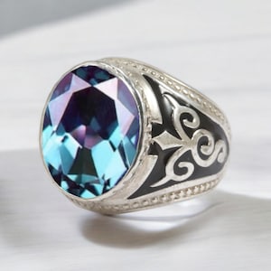 Peut inclure: Une bague en argent ornée d'une grosse pierre ovale aux tons bleus et violets. La bague présente un motif en émail noir sur les côtés avec un motif décoratif.