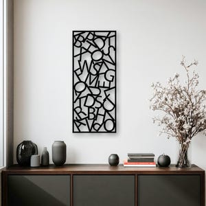 May include: A rectangular black metal wall art piece featuring a cutout design of various overlapping uppercase letters arranged in a dense, vertical pattern. The letters are interconnected, creating a continuous, open-work structure.