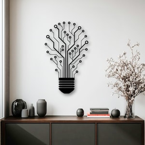 Puede incluir: Arte de pared de metal negro con forma de bombilla, con un diseño de placa de circuito. La obra de arte está montada en una pared blanca sobre un mueble de madera oscura. El diseño incorpora líneas y círculos, creando una estética moderna inspirada en la tecnología.