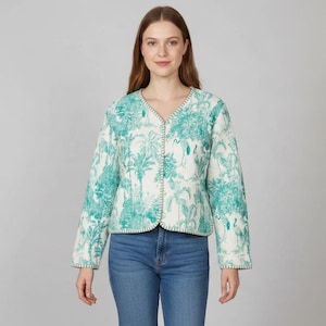 May include: A long-sleeve quilted jacket featuring a teal and white tropical toile pattern with palm trees and birds. The jacket has a V-neckline, a button-front closure, and a straight hemline, paired with blue denim jeans.