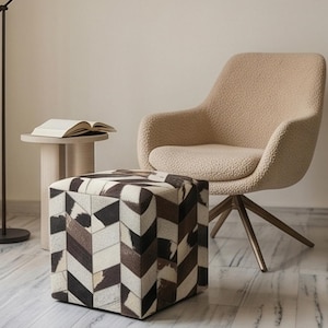 Può includere: Una poltrona beige testurizzata con base girevole, un pouf quadrato con motivo a chevron nero, bianco e marrone, e un piccolo tavolino rotondo con un libro aperto, accompagnati da una sottile lampada da terra nera dal collo slanciato.