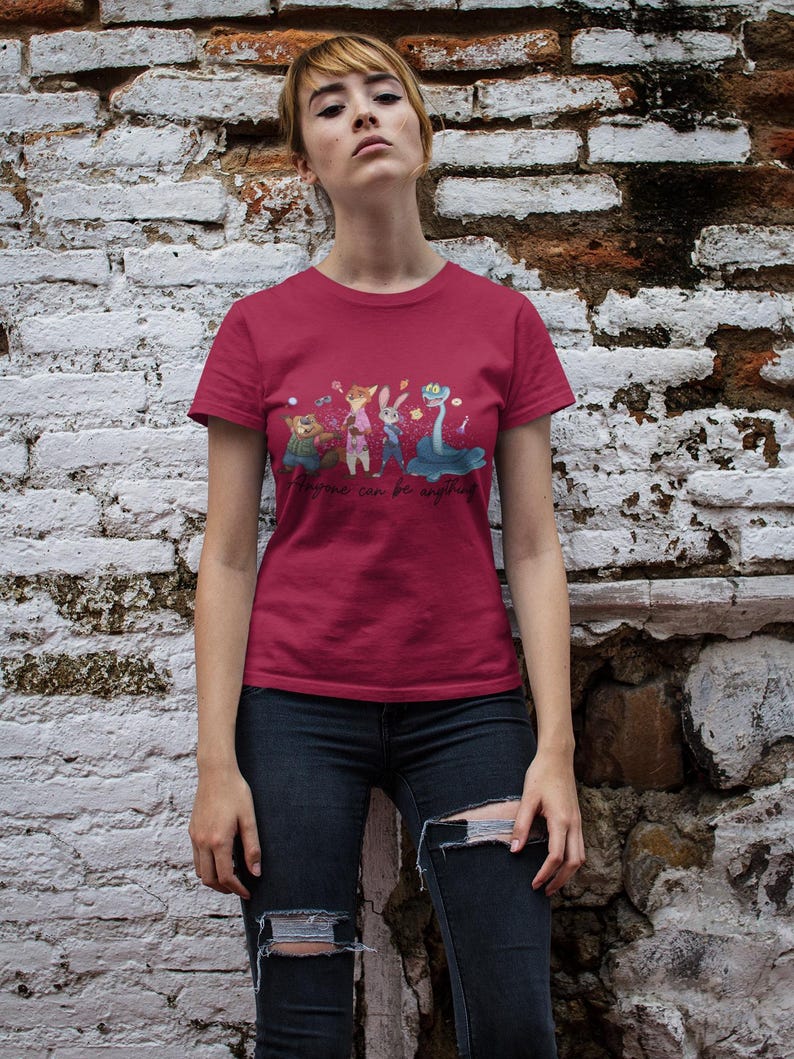 Pu&ograve; includere: Una t-shirt a maniche corte rosso scuro con una stampa grafica di quattro personaggi animali animati e il testo "Anyone can be anything" in carattere corsivo. La maglietta ha un girocollo e un orlo dritto in tessuto a tinta unita.