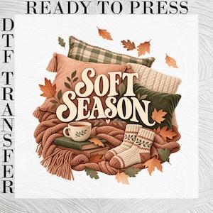 May include: A DTF transfer design featuring the text SOFT SEASON in cream lettering, surrounded by a collection of pillows in plaid, solid peach, and green, a pair of knit socks, two stacked books, a mug, and scattered autumn leaves.