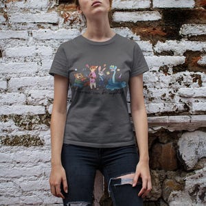 Pu&ograve; includere: Una t-shirt a maniche corte grigio scuro con una stampa grafica di quattro personaggi animati, tra cui un castoro, una volpe, un coniglio e un serpente. Sotto i personaggi, il testo "Anyone can be anything" &egrave; scritto in un carattere corsivo nero.