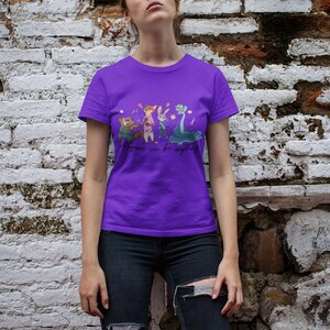 Pu&ograve; includere: Una t-shirt viola a maniche corte con una stampa grafica di quattro personaggi animati, tra cui una volpe, un coniglio e un serpente, con il testo "Anyone can be anything" stampato in corsivo nero al centro della zona del petto.