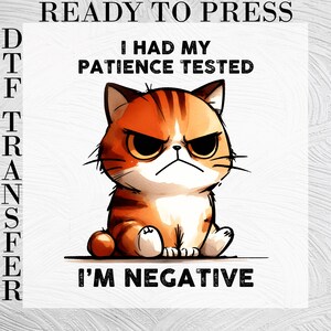 May include: A DTF transfer featuring an orange tabby cat with a grumpy expression. The text reads READY TO PRESS at the top, I HAD MY PATIENCE TESTED in the middle, and I'M NEGATIVE at the bottom. The cat has dark stripes and large eyes.