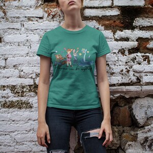 Pu&ograve; includere: Una t-shirt a maniche corte color verde acqua con una stampa grafica di quattro personaggi animati e il testo "Anyone can be anything" in corsivo. La maglietta presenta un girocollo e un orlo dritto con un'illustrazione colorata.