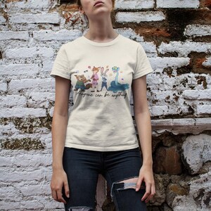 Pu&ograve; includere: Una t-shirt a maniche corte color crema con una stampa grafica di quattro personaggi animali animati e il testo "Anyone can be anything" scritto in corsivo sotto i personaggi. La maglietta ha un girocollo e un orlo dritto.