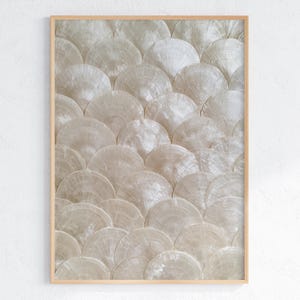 Peut inclure: Une œuvre d'art murale rectangulaire présentant un motif répétitif de disques de coquillages blancs irisés superposés en forme d'écailles, le tout encadré par un cadre en bois clair simple aux bords droits et nets.