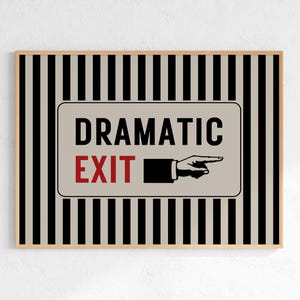 Puede incluir: Arte mural enmarcado con fondo beige y rayas verticales blancas y negras. La obra presenta un letrero que dice "DRAMATIC EXIT" con un gráfico de mano que señala. El marco es de color madera clara.