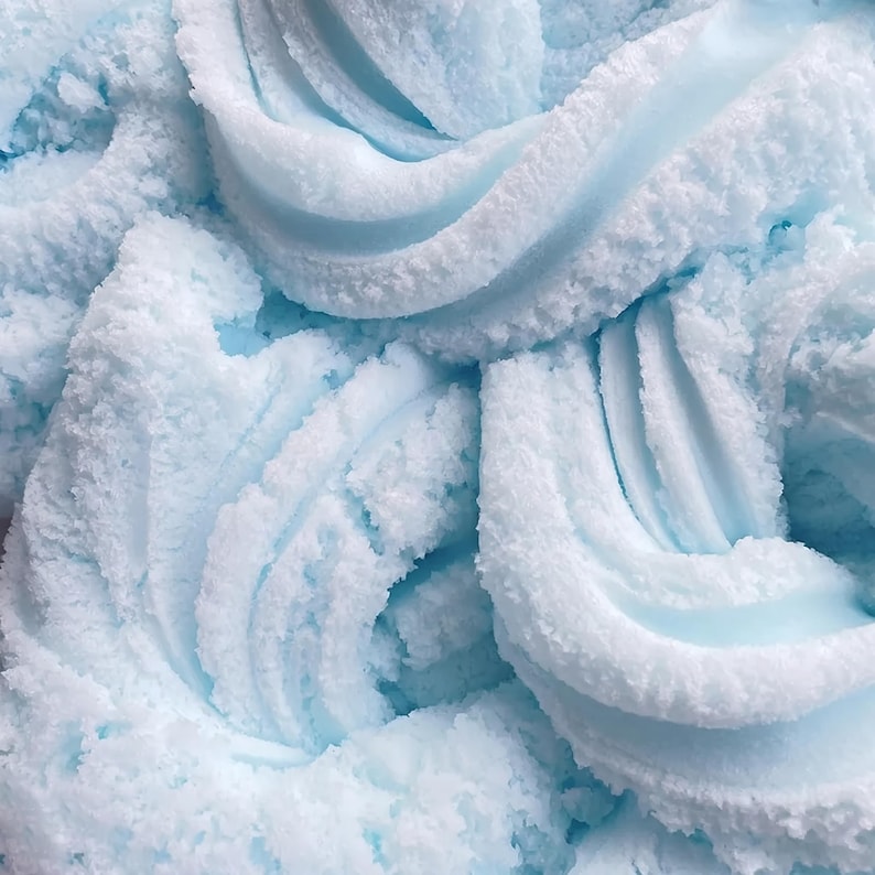 May include: Close-up of a light blue, textured substance with a fluffy, cloud-like appearance. The material has a soft, almost whipped texture, with a slightly granular surface. The color is a pale, pastel blue, creating a soothing visual effect.