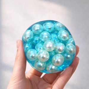 以下が含まれることがあります： 黒い持ち手と「But First, Coffee」の文字が黒い手書き風フォントで書かれた白いセラミックマグ。マグカップは白い表面に置かれています。