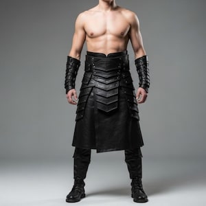 Op de afbeelding: Een zwarte leren kilt met bijpassende armbeschermers en laarzen. De kilt heeft gelaagde panelen en een brede riem. De armbeschermers hebben een ge-stud design. De laarzen zijn zwart en vetersluiting.
