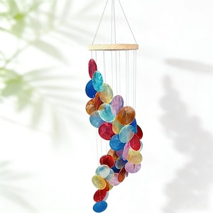 Puede incluir: Un carillón de viento colorido con una parte superior de madera y numerosos elementos ovalados iridiscentes en varios colores. Las piezas, en tonos de rojo, azul, naranja y amarillo, están suspendidas por cuerdas.