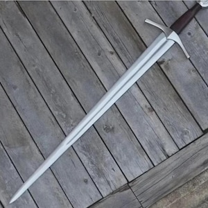Peut inclure: Une longue épée dotée d'une lame en acier à double tranchant, d'une garde droite argentée et d'une poignée enveloppée de cuir brun foncé. Le pommeau est arrondi et métallique, complétant la monture de cette arme à lame droite.