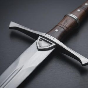 May include: A detailed view of a medieval sword. The blade is polished steel, and the handle is dark brown wood with silver detailing. The sword has a crossguard and a shield-shaped design near the blade. The overall design is historical.