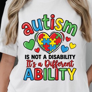 May include: A black t-shirt and a white t-shirt, each featuring a colorful graphic with the text 'autism IS NOT A DISABILITY It's a Different ABILITY' above a heart shape filled with multi-colored puzzle pieces and small heart icons.