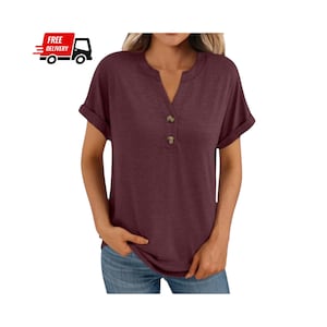 May include: Burgundy short-sleeve Henley shirt with a V-neckline and two brown buttons. The shirt has rolled-up sleeves and is made of a soft, comfortable material. The shirt is paired with blue jeans.
