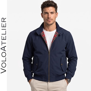 May include: A navy blue zip-up jacket featuring a stand-up collar, ribbed cuffs and hem, two front flap pockets with buttons, and a red, green, and white tartan plaid lining. The text VOLOATELIER is printed vertically on the left side of the image.