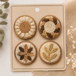 Pode incluir: Um conjunto de quatro broches circulares de madeira com bordado texturizado em tons de bege, areia e castanho. Cada broche apresenta um design botânico único, incluindo um girassol, uma coroa, uma flor em forma de estrela e um ramo.