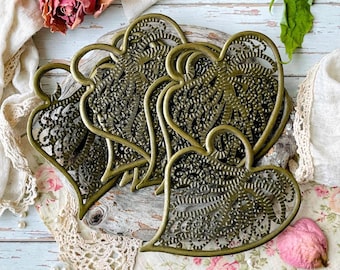 Può includere: Una collezione di quattro ciondoli in metallo a forma di cuore color ottone antico, caratterizzati da un intricato motivo a filigrana traforata con superficie testurizzata. Ogni cuore presenta un piccolo occhiello circolare sulla parte superiore.