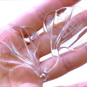 Peut inclure: Deux embellissements en verre transparent en forme de fleur avec une surface textur&eacute;e. Les embellissements sont tenus dans une main.