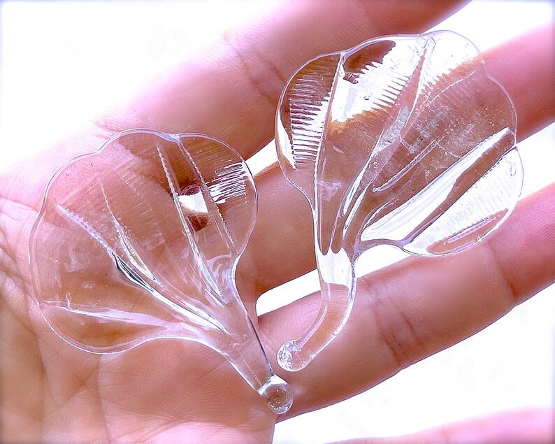 Peut inclure: Deux embellissements en verre transparent en forme de fleur avec une surface textur&eacute;e. Les embellissements sont tenus dans une main.