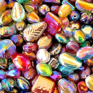 K&ouml;nnte beinhalten: Eine Sammlung von irisierenden Glasperlen in verschiedenen Formen und Gr&ouml;&szlig;en, darunter Tropfen-, Oval- und quadratische Formen. Die Perlen haben einen regenbogenartigen Glanz und eignen sich perfekt f&uuml;r die Schmuckherstellung oder das Basteln.
