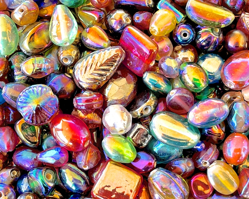 K&ouml;nnte beinhalten: Eine Sammlung von irisierenden Glasperlen in verschiedenen Formen und Gr&ouml;&szlig;en, darunter Tropfen-, Oval- und quadratische Formen. Die Perlen haben einen regenbogenartigen Glanz und eignen sich perfekt f&uuml;r die Schmuckherstellung oder das Basteln.