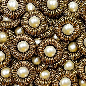 May include: Close-up of a collection of gold-toned buttons with a pearl center. The buttons have a decorative, rope-like design around the edges.